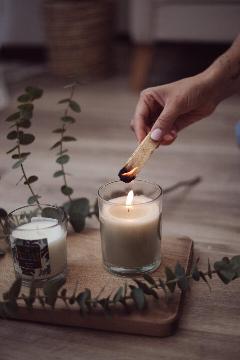 Mano femminile che accende una candela con un fiammifero, luce calda e atmosfera intima. Fotografia editoriale di personal branding per professioniste del benessere.