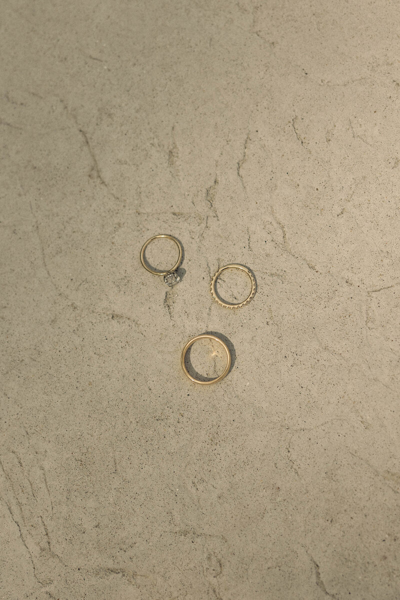 Minimalist shot of three wedding rings laid on a textured concrete surface, symbolizing the enduring bond and commitment of marriage