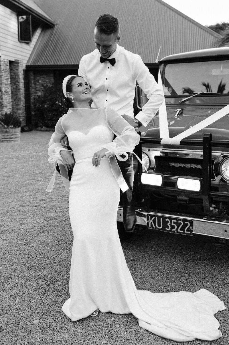 black and white photo of bride and groom sitting on a land rover in trish peng gown at their christchurch backyard wedding