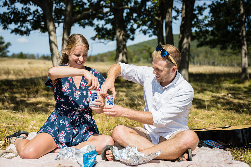 A couple on their elopement day excitedly open a can of PBR as they prepare for their elopement picnic in Shenandoah National Park at Big Meadows.
