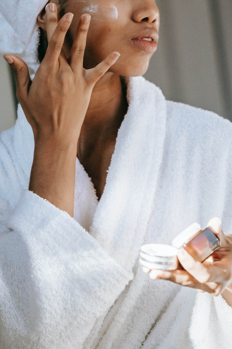 Woman in robe putting on facial moisturizer | St. Pete Rejuvenate Medspa and Infusion Center