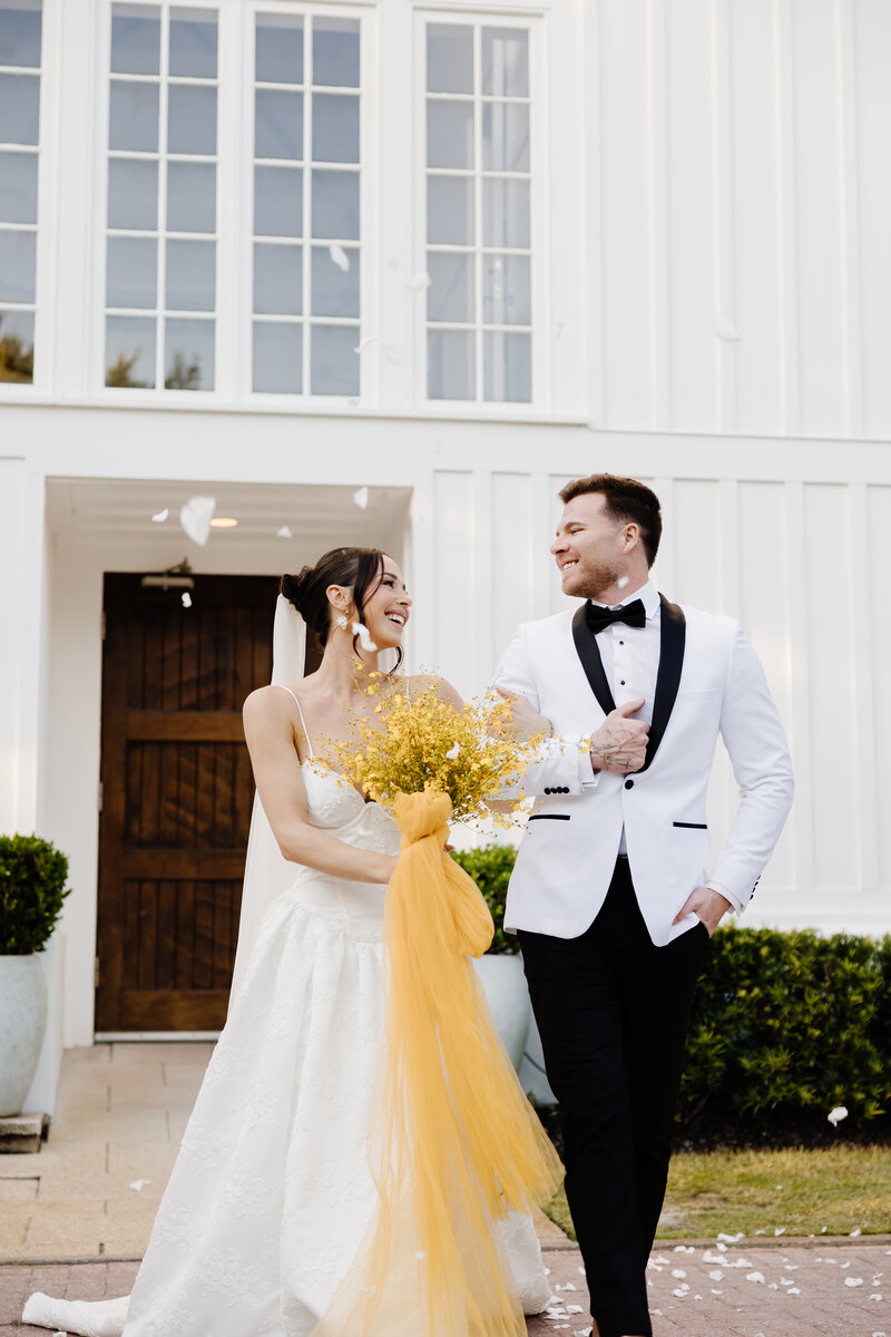 A newlywed couple walking out of a church under flower petals