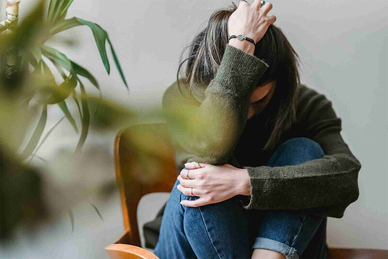A woman sits on a chair, hands on her head, expressing feelings of anxiety and stress in a quiet moment of reflection.