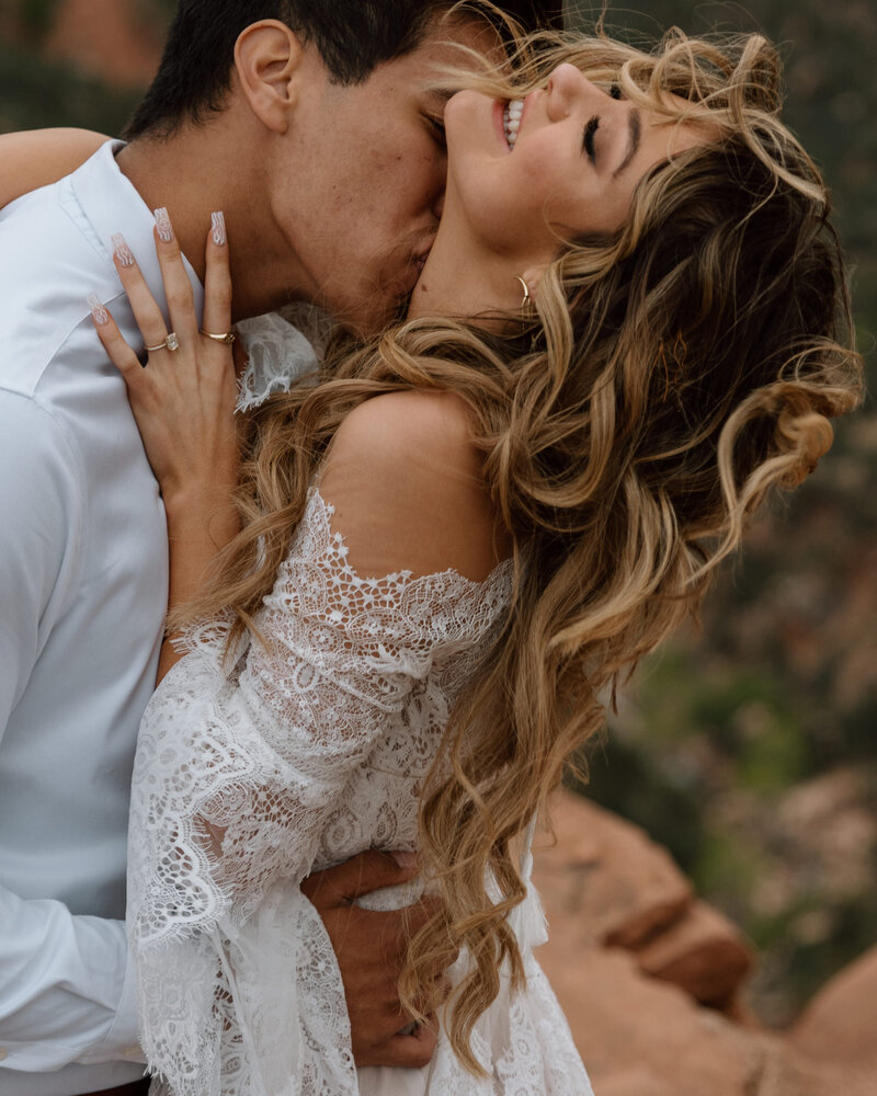 groom kissing the brides neck while the wind blows her curly hair on Zion Overlook