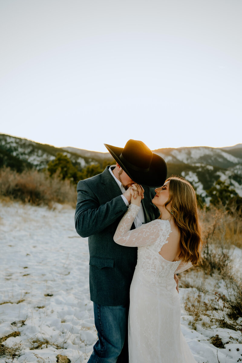 groom kissing brides hand with snowy mountains in the background