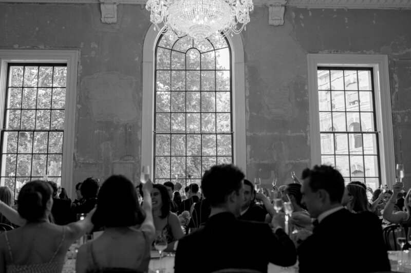 Black-and-white image of guests enjoying candlelit dinner under chandeliers.