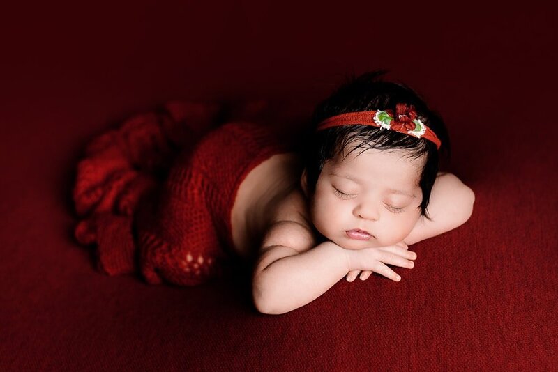 Newborn baby girl in dark red chin on hands beanbag pose