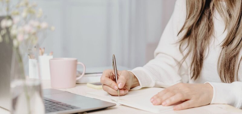 Woman writing while sitting at laptop