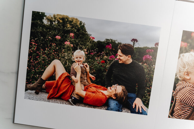A photo album lying on a marble table, open to a page featuring a family enjoying time together in a garden.