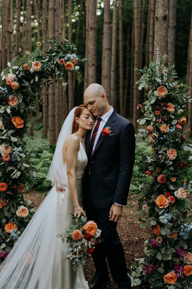 A bride and groom share a private moment in front of their woodland wedding ceremony arch.