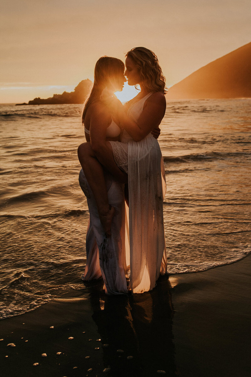 Elopement Photography, couple standing at the water's edge with sunset behind them