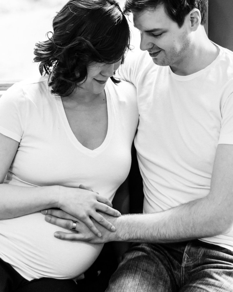 Pregnant couple hold hands on belly expectantly