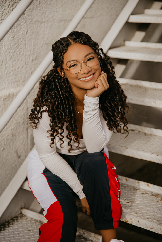 girl with long curly hair and glasses smiling on staircase