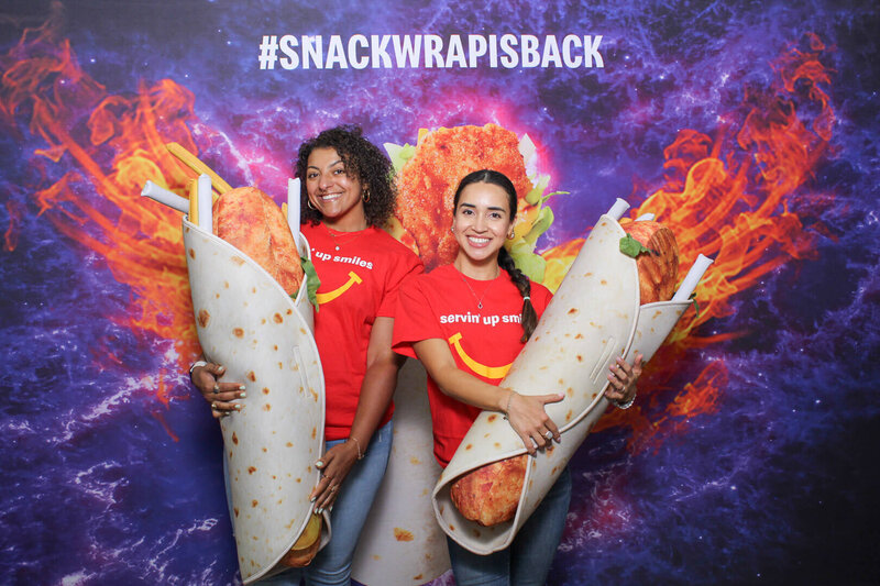 Two guests posing with oversized snack wrap props in front of a custom McDonald’s backdrop with the hashtag Snack is wrap captured by Philly Snap Booth during a multi-day brand activation event.
