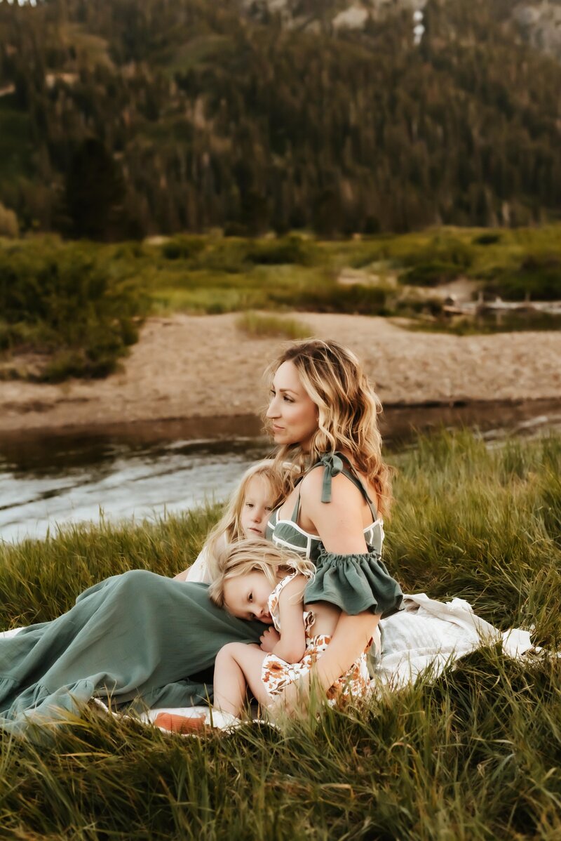 Mother in a gorgeous green dress sitting with her two young daughters in Olympic Valley Meadows.