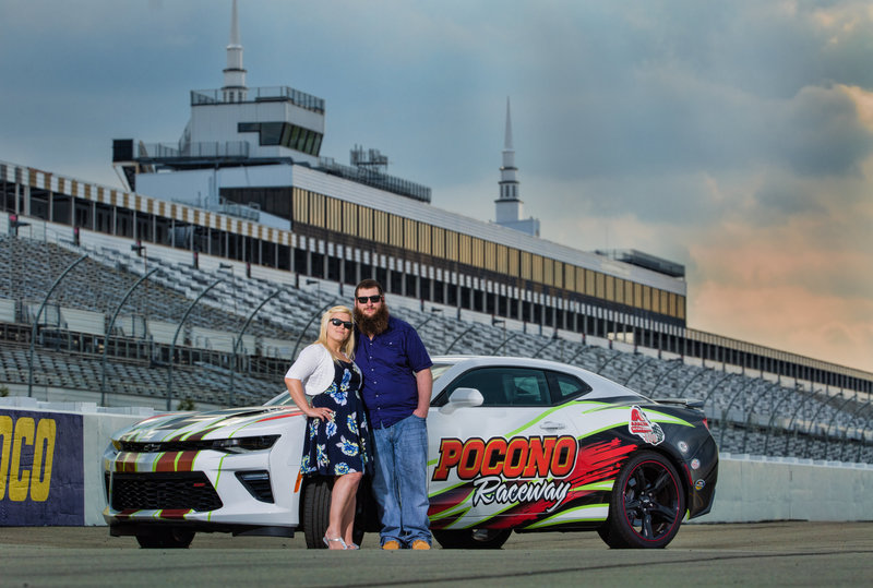Engaged couple standing together on the track at Pocono Raceway, blending their love of motorsports with their engagement session.