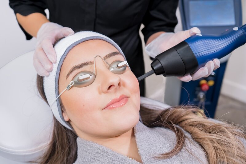 Closeup image of a woman lying down getting microneedling treatment from an esthetician with hot pink gloves
