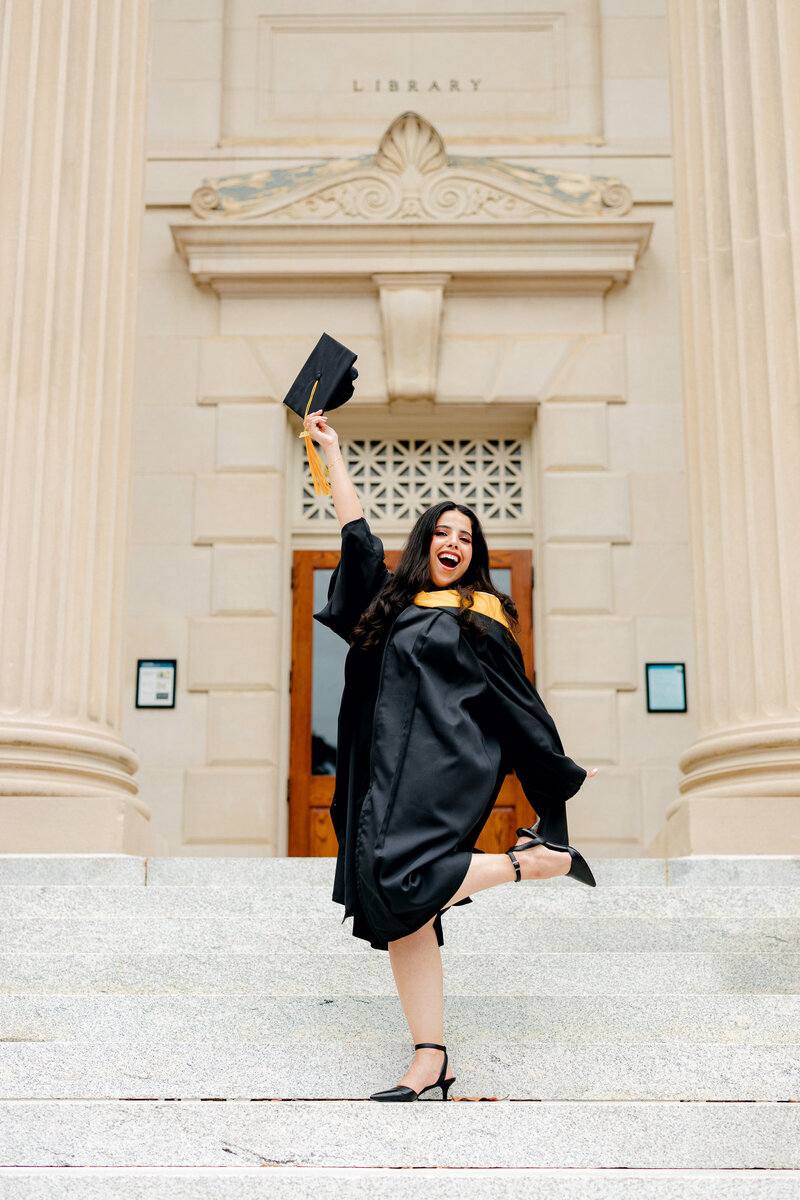 Graduate popping foot while wearing gown and holding cap in the air.