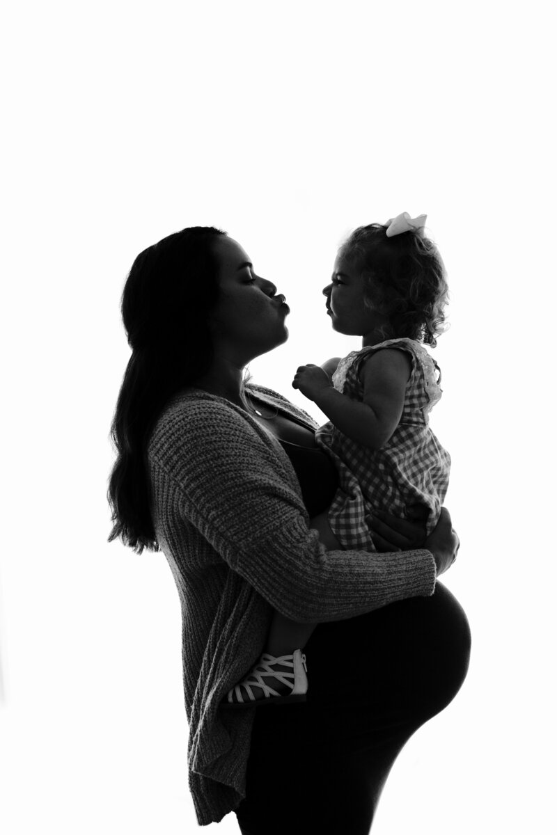 Silhouetted black and white image of a pregnant mom holding her child
