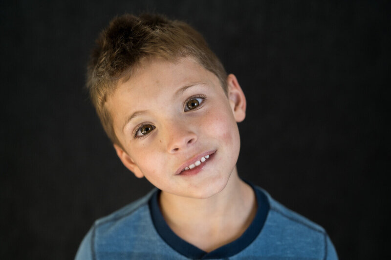 A school aged boy tilts his head and looks intently and curiously into the camera on school picture day with Kate Simpson Photography in Minnesota.