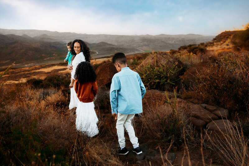 mom holding her toddler while children follow during golden hour family session in Scottsdale