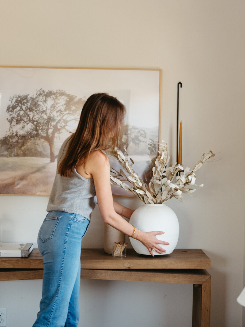 Interior designer Natalie Barnas styling a minimalist console table with dried floral arrangement in a neutral-toned San Diego home.