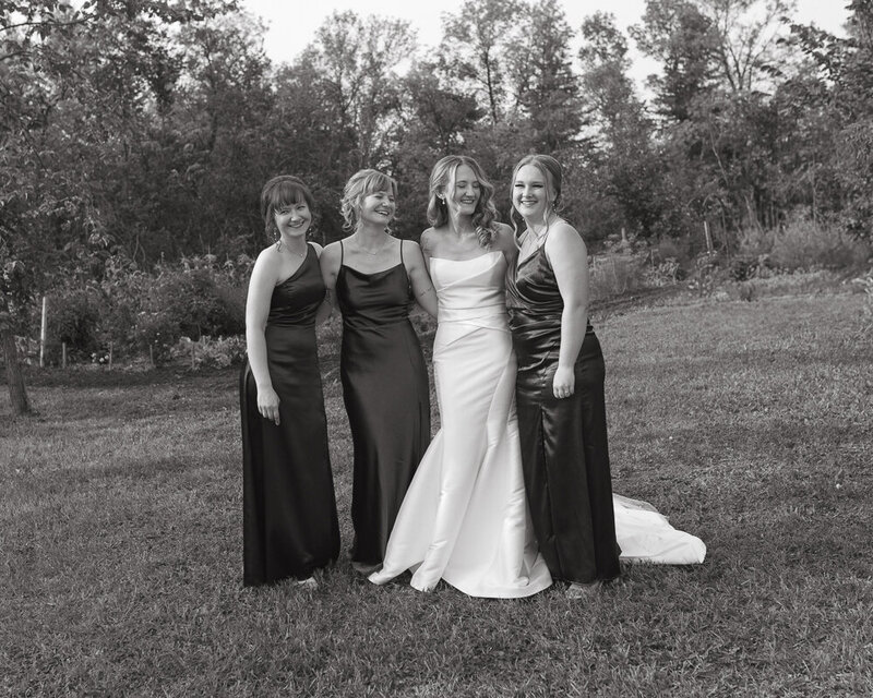 A joyful bride stands with her bridesmaids in elegant satin dresses during an intimate wedding celebration in Tisdale, Saskatchewan.