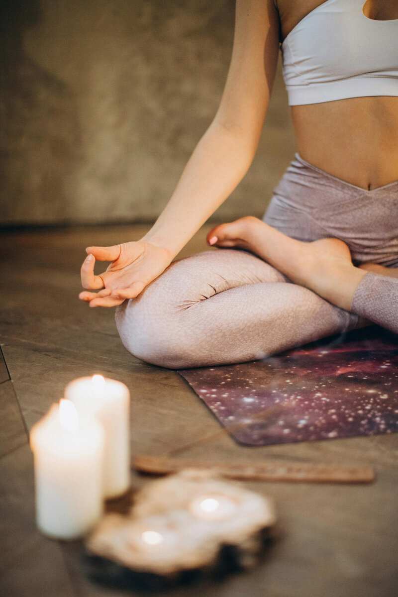 Woman meditating on a yoga mat next to burning candles