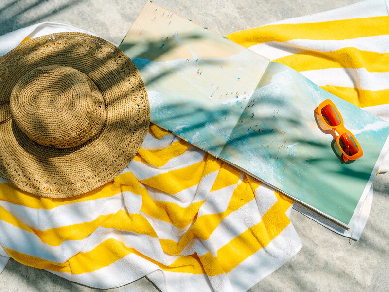 Book, straw hat, and orange sunglasses laying on a yellow striped towel