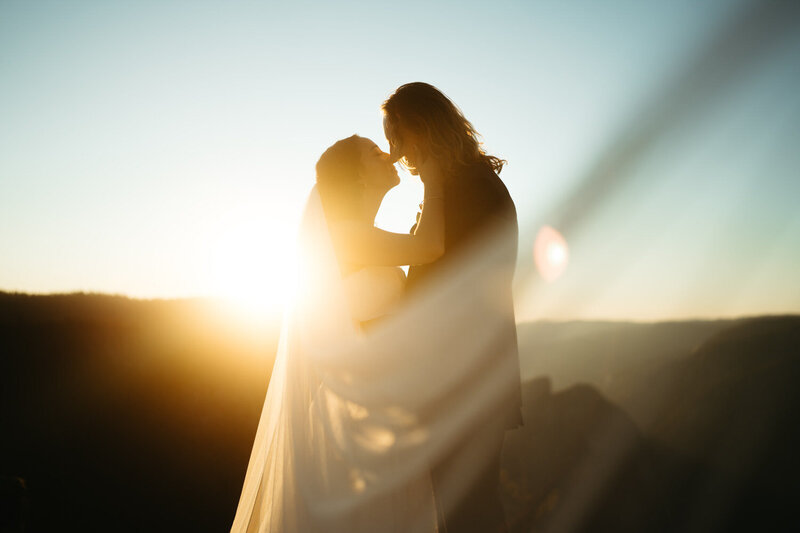 Close up photo of a Yosemite elopement, groom is holding brides face to kiss her with a sun flair and Half Dome behind them