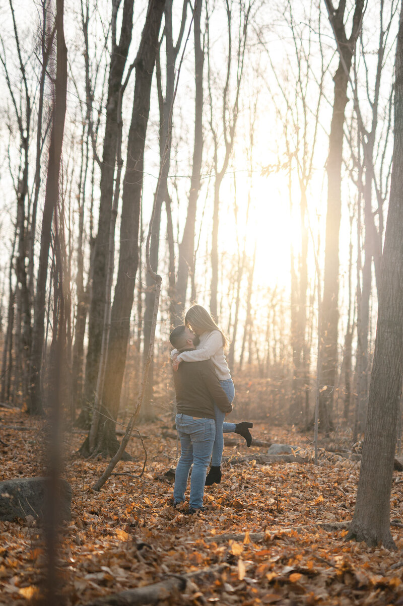 Fiancé porte sa fiancée dans la forêt lors d'une séance de fiançailles au Golden Hour à Laval