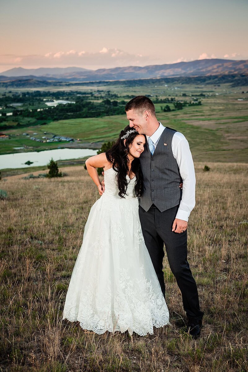 Bride and groom standing on a hilltop with the Montana valley and mountains behind them at sunset