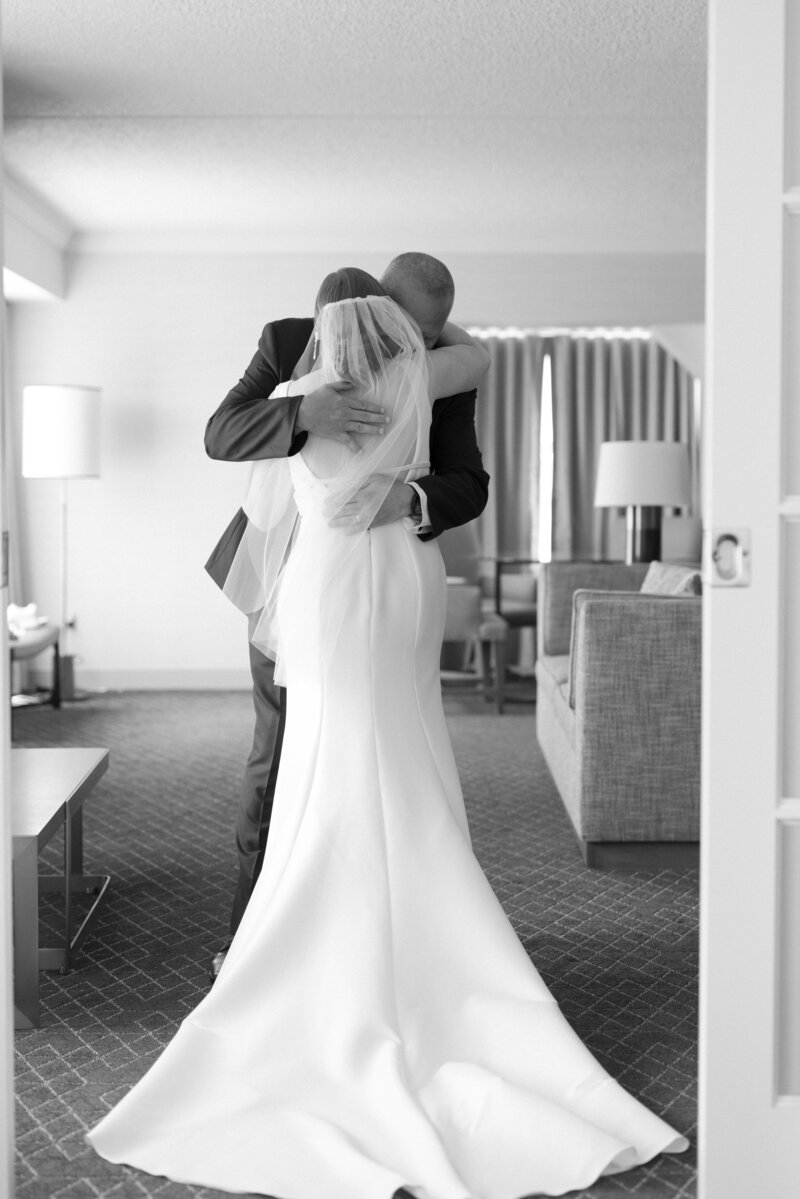 A dad hugs his daughter after emotional first look of her in her bridal gown in Black and White image taken by wedding photographer in Illinois Lacey Graham