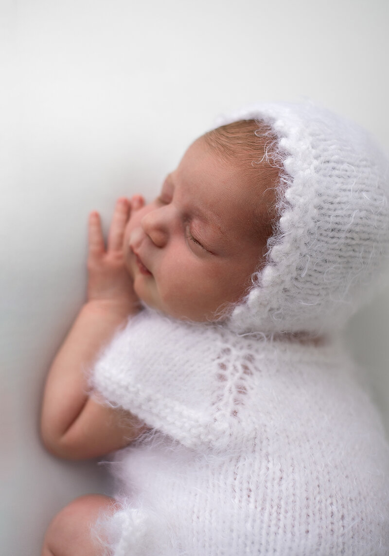 newborn baby wearing a white bonnet and outfit on a white blanket