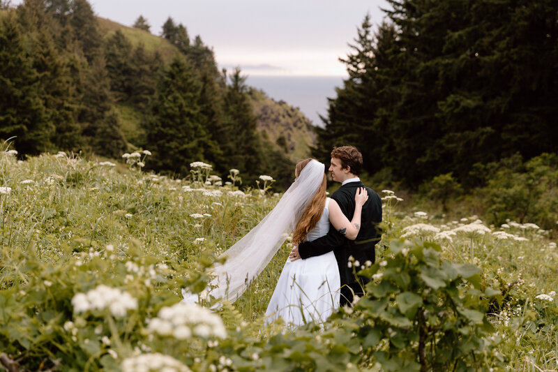 Bride and groom embracing while standing in a meadow on the Oregon Coast.