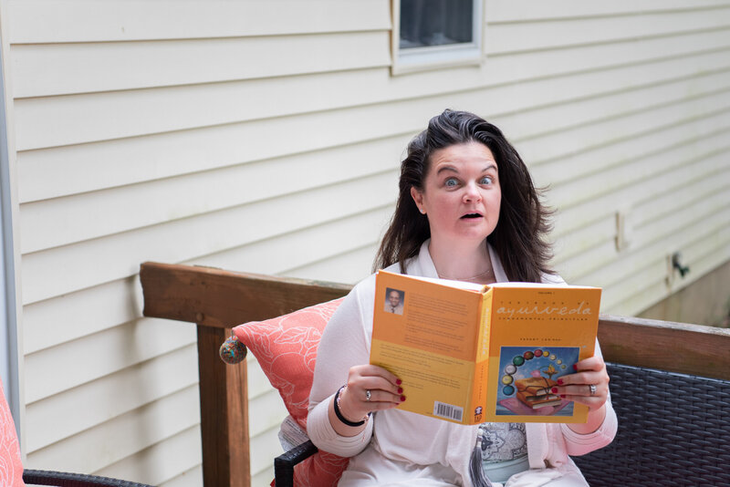 A woman sitting outside with a surprise look while holding an Ayurveda book.