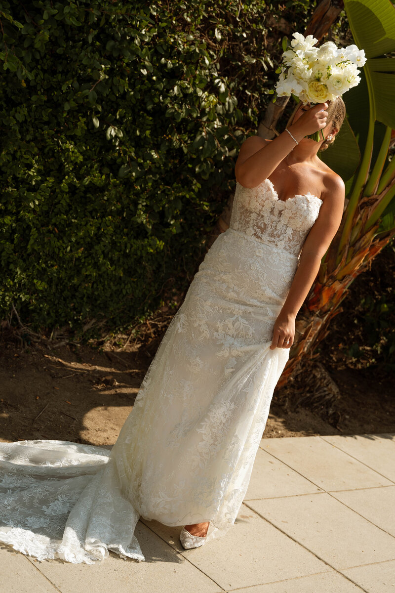 a bride's dress and her holding a bouquet in front of her face
