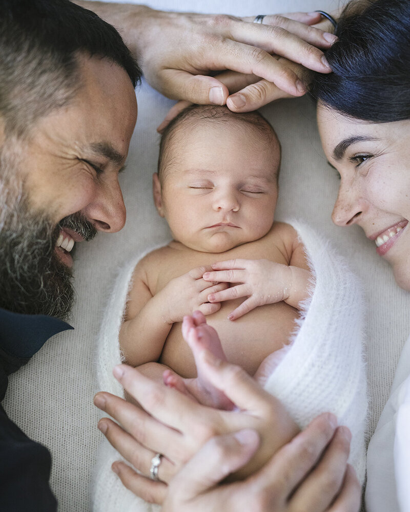 husband and wife, snuggling and looking at their newborn up close and the newborn is swaddled, Perth newborn in home session