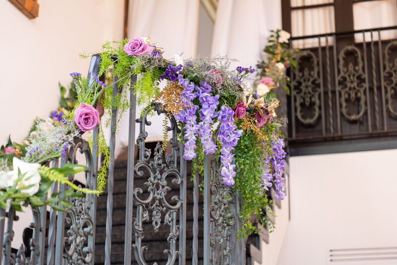 The floral centerpiece on the stairs with white, purple, and pink flowers at a reception celebration event.