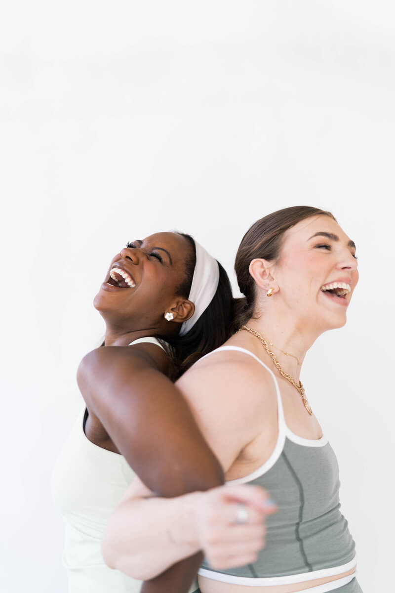 two women back to back laughing