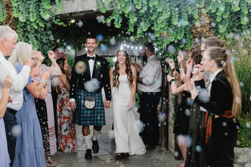 A bride and groom exit their wedding while guests blow bubbles