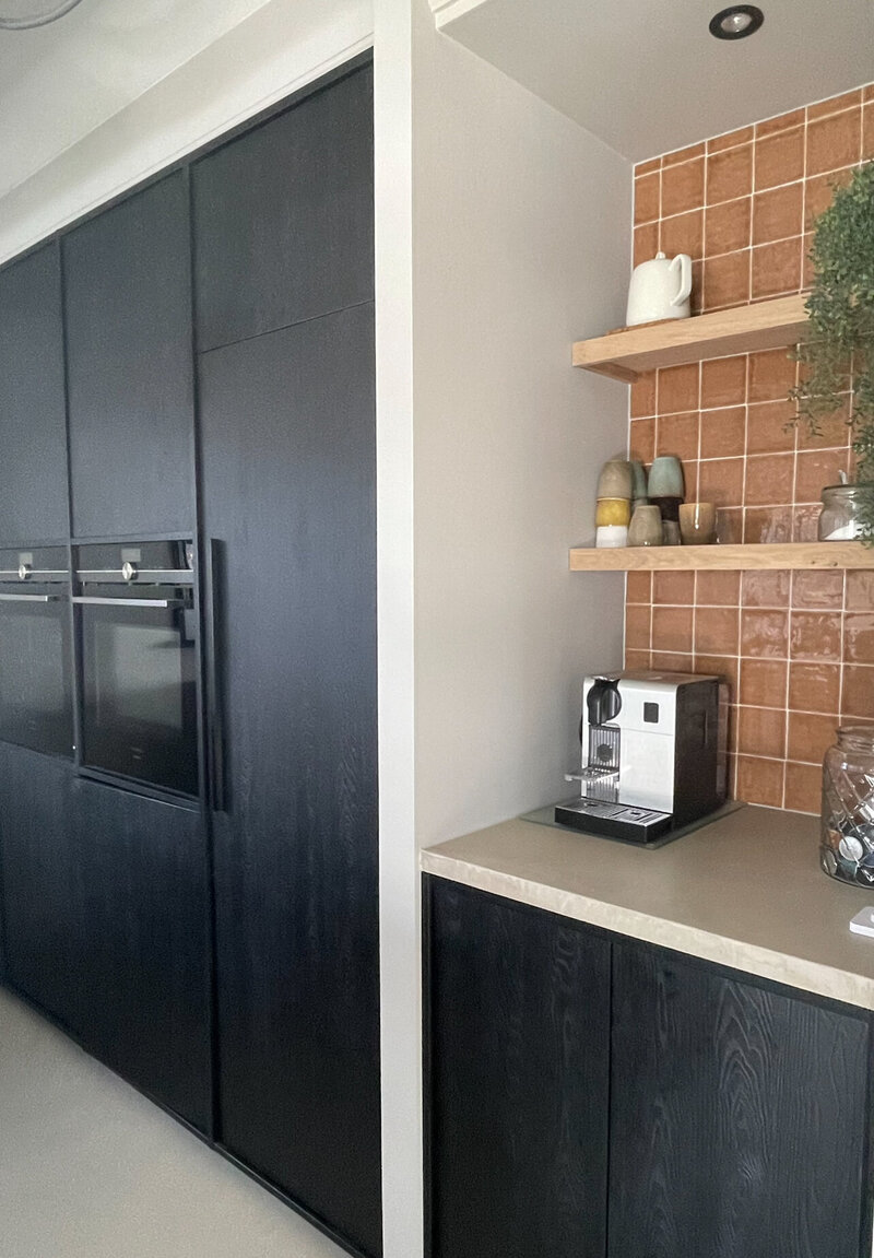 Strakke keuken met zwarte kasten, open houten planken en een warm accent van terracotta tegels.