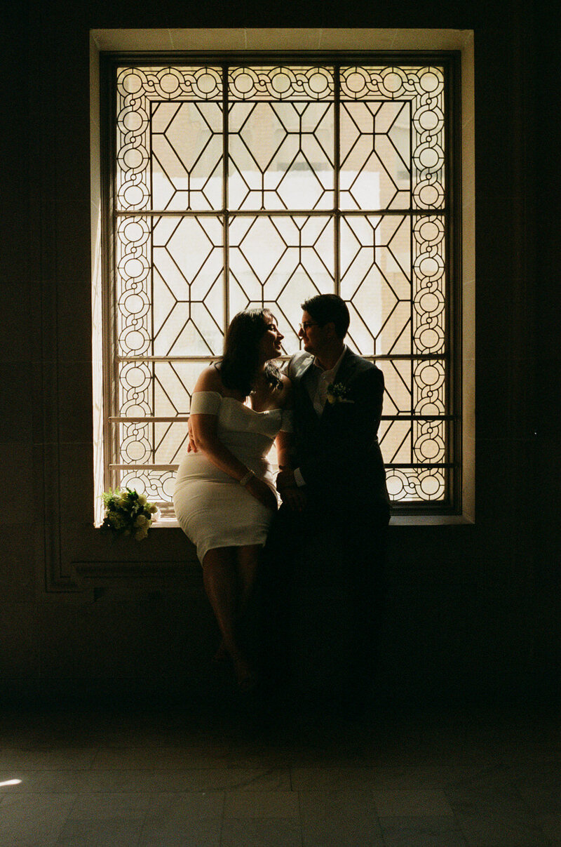 photo of bride and groom sitting in large windows at san francisco city hall