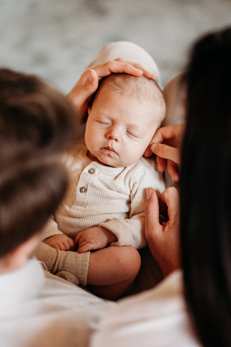 Baby ligt in de armen van de ouders te slapen tijdens een fotoshoot.