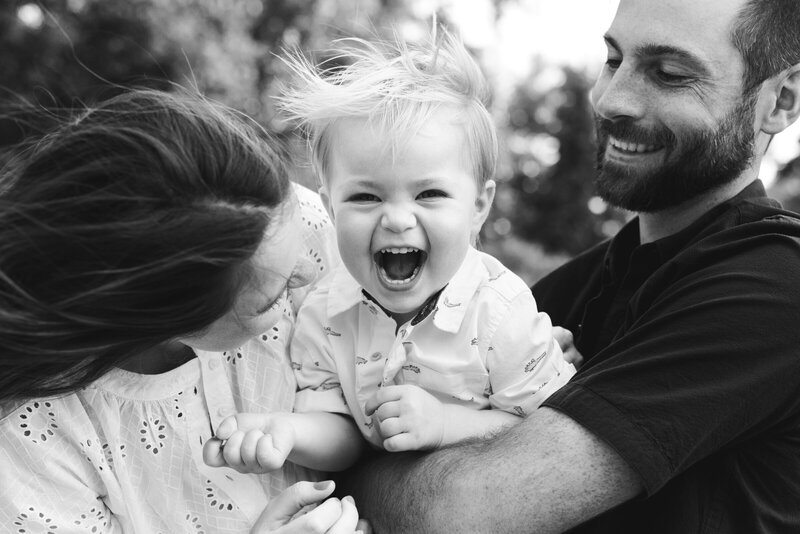 black and white photo of parents making toddler boy laugh
