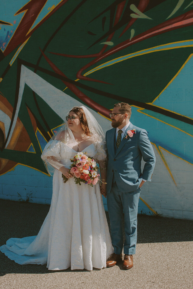 bride and groom pose on a bench in front of rose bush