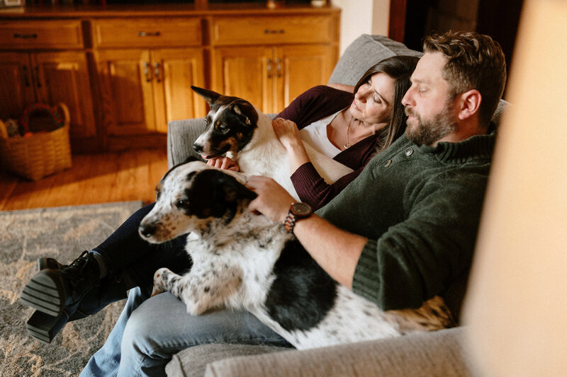 A happy couple cuddles with their dog on a cozy couch, enjoying a relaxing moment together at home.