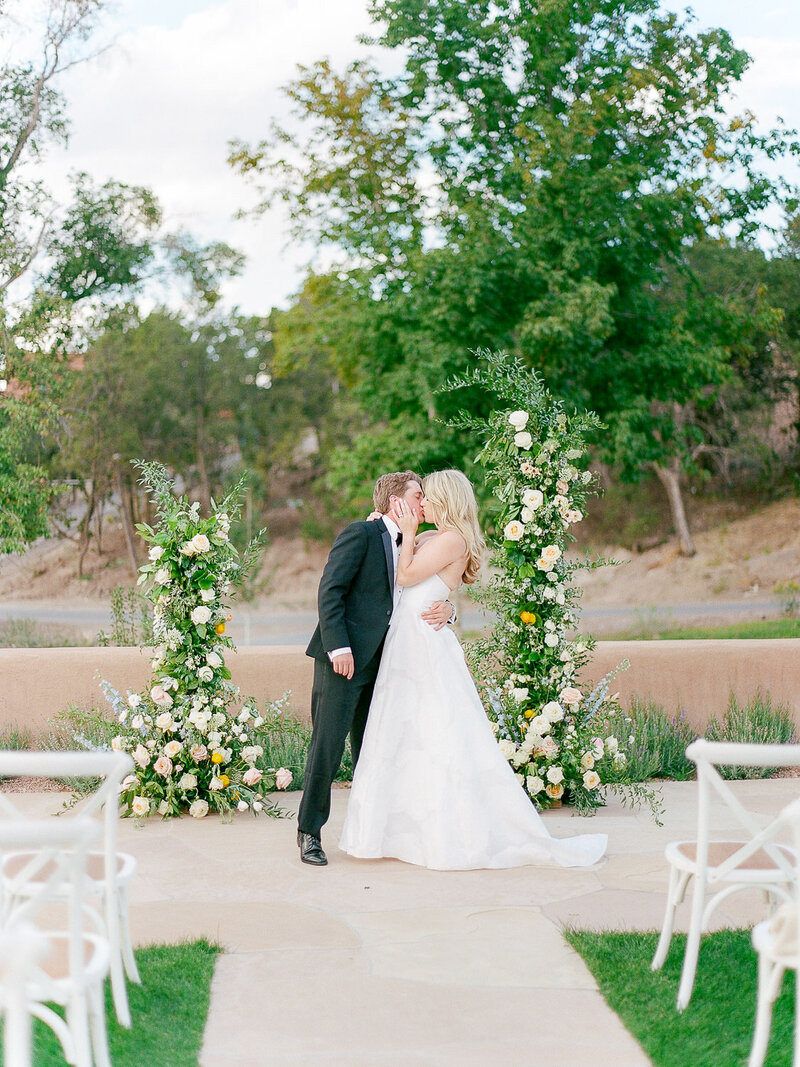 Bride and groom kiss under floral wedding ceremony arch at Bishop's Lodge in Santa Fe