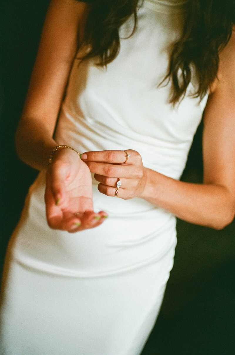 Faceless photo of bride in sleek, simple white dress, focused on hands clasping bracelet