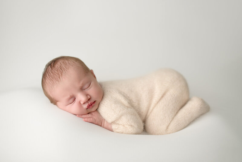 Newborn posed session, baby girl in the tushie up pose on white background wearing a soft knit romper
